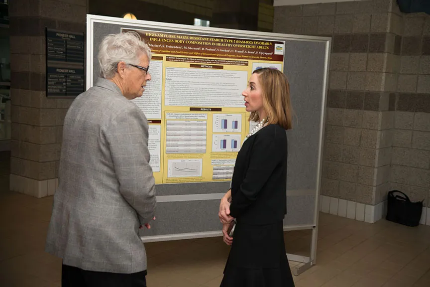 a man and woman stand and discuss a scientific presentation poster