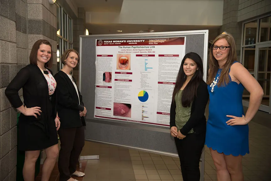 four women pose in front of a scientific presentation poster