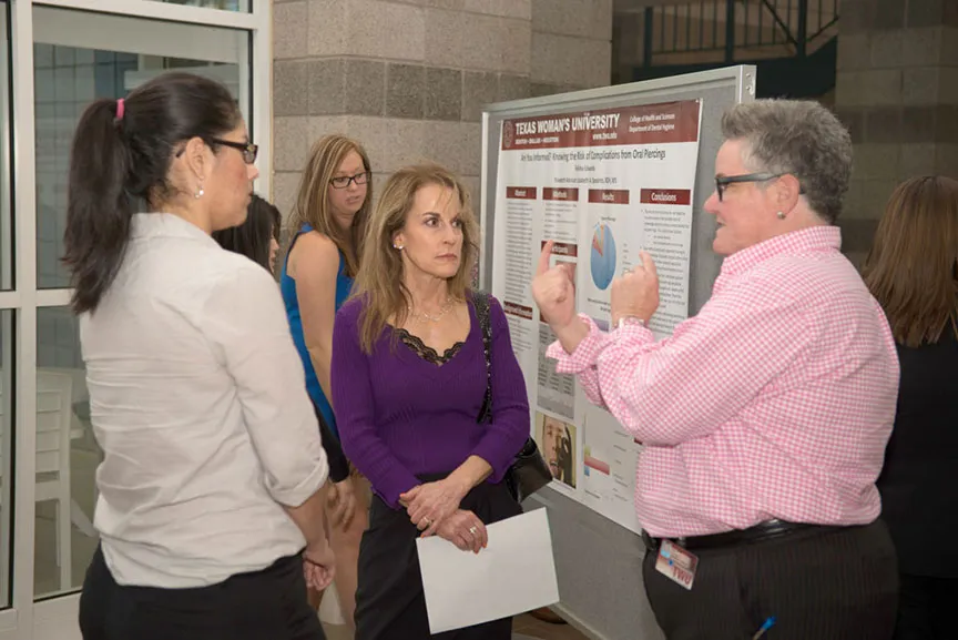  a woman explains her presentation poster to a group of people