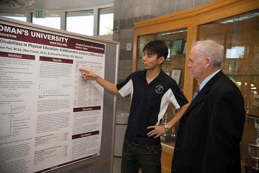 a young man explains his presentation poster to an onlooker