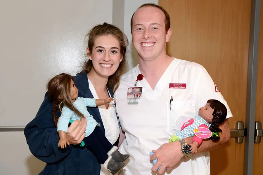 Two nursing students pose together with dolls for pediatric patients