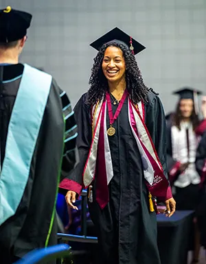 A student walks the stage at Commencement wearing the scholar medallion with her academic regalia
