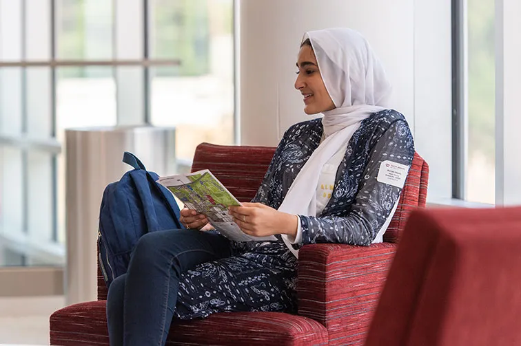 A young women wearing a head scarf looks through an orientation handout with campus map