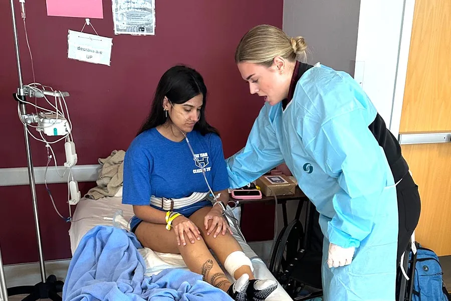 a student in blue scrubs stands over a patient in a blue shirt on a hospital bed