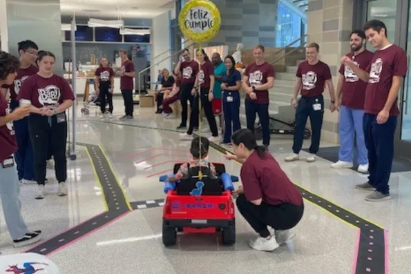 a student crouches next to a child sitting in a small robotic car