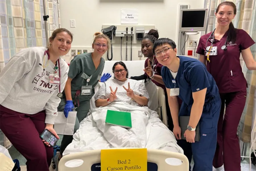 five TWU students dressed in different colored scrubs stand around a hospital bed and a patient