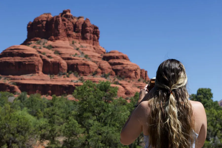 Angel Trosper standing in front of Bell Rock and taking a photo of the rock formation.