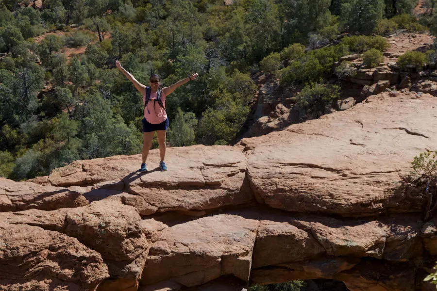 Mayra Peralta standing with her arms outstretched on Devil's Bridge Trail with a canyon behind her.