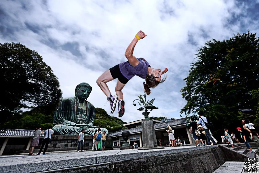 Luci Romberg mid backflip in a Japanese garden with Buddha in the background.