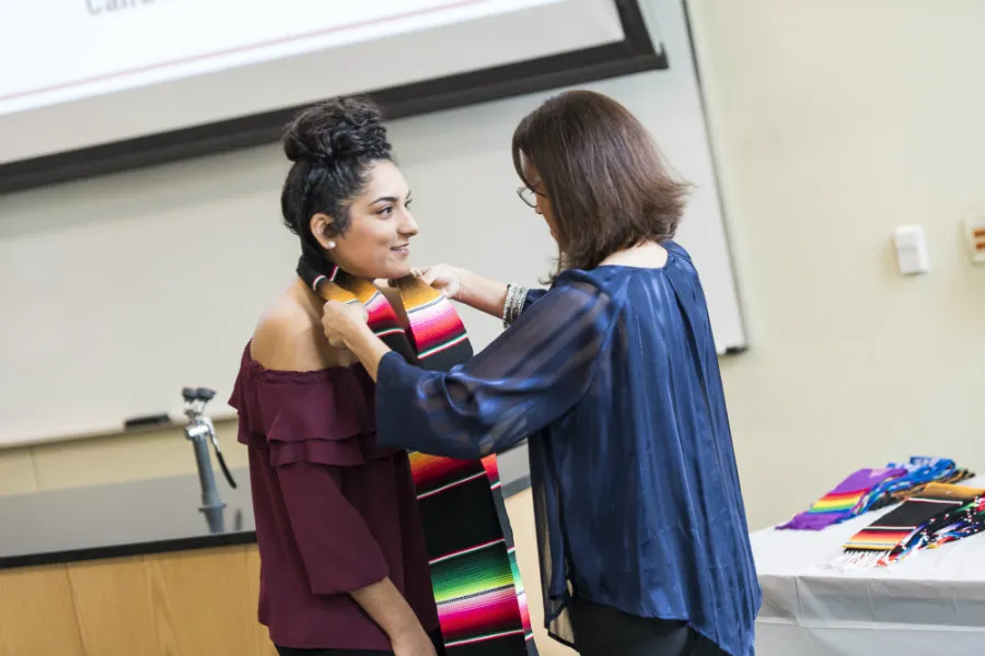 Becky Rodriguez placing a Raza Stole around the neck of a TWU student she mentored at the Multicultural Graduation event. 