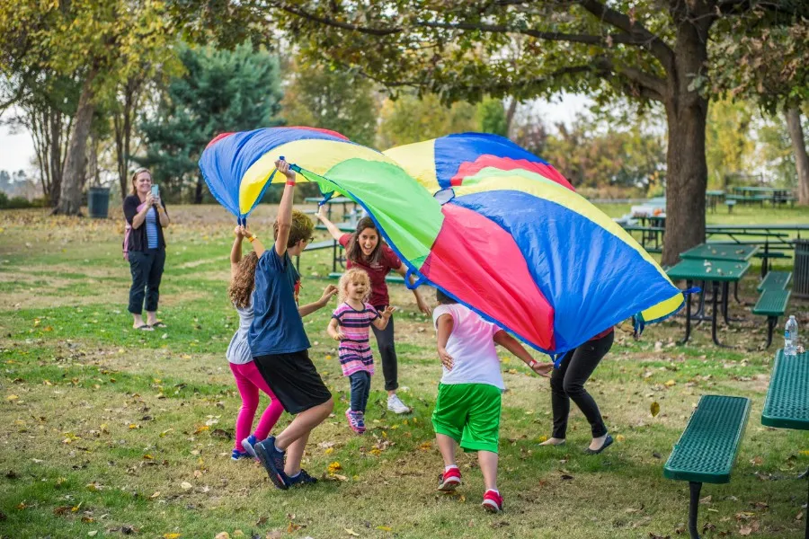 A TWU student playing with a group of young kids under a parachute at the Dallas Arboretum.