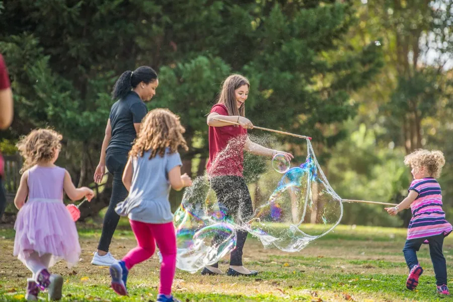 A TWU student playing with a bubble machine with young kids at the Dallas Arboretum.