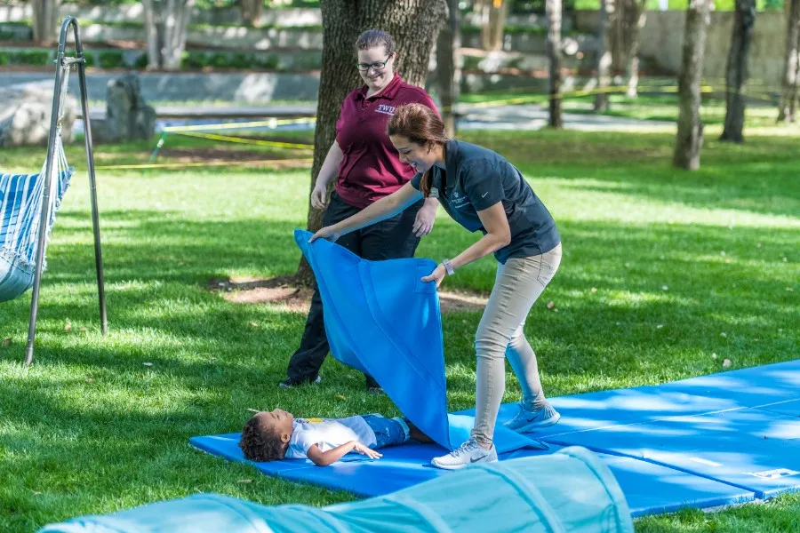 Two TWU students place a weighted blanket on a young child at the Nasher Sculpture Museum.