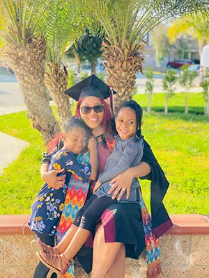 Kwashae Ruffin in a graduation cap and gown smiles with her two children