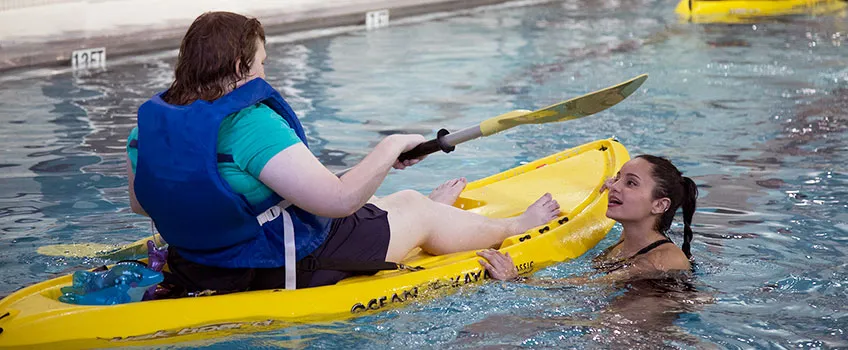 Student practicing kayak skills in the indoor pool while another student looks on. 
