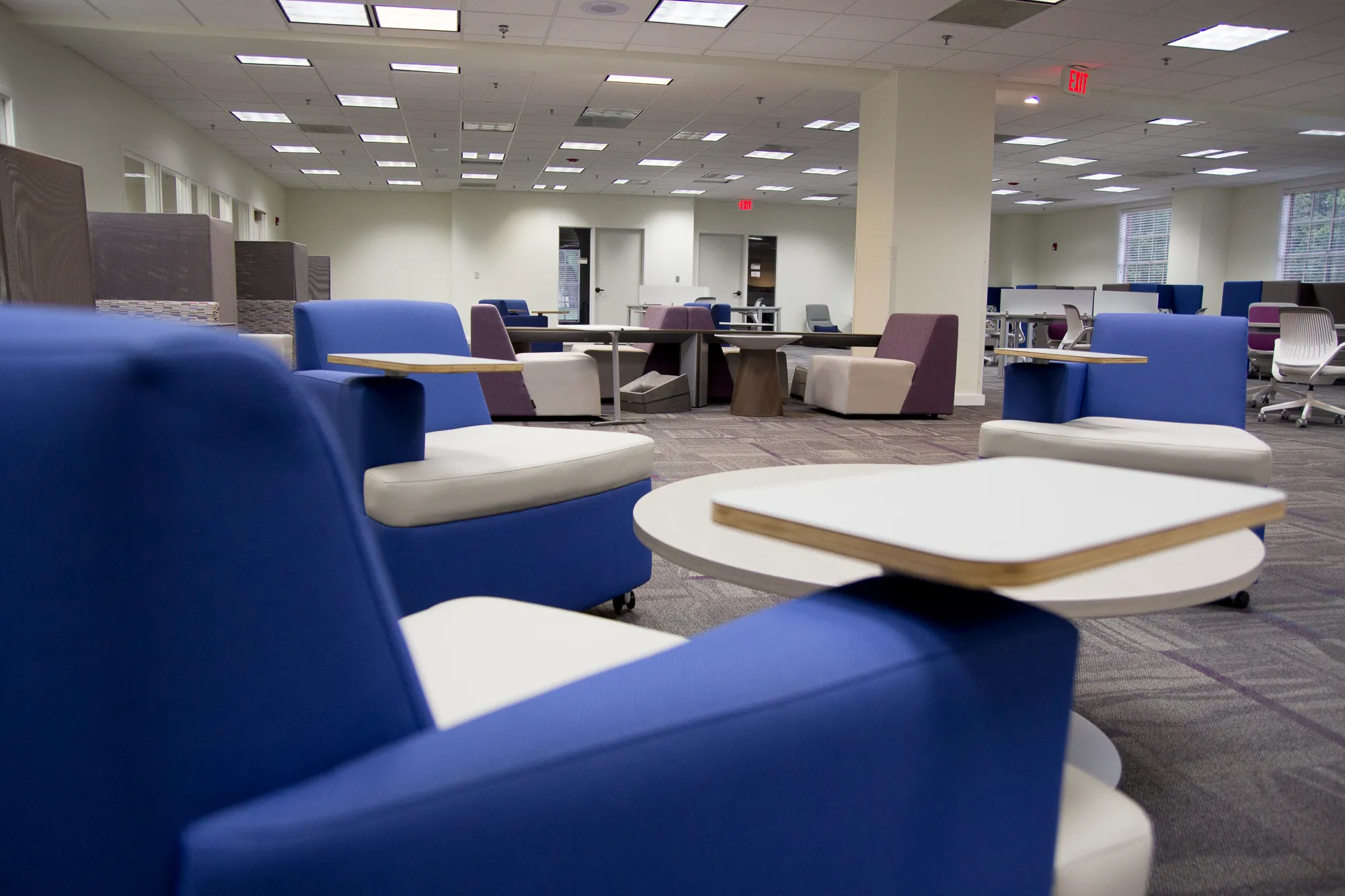 Modern study space with blue chairs, white tables, and bright lighting.