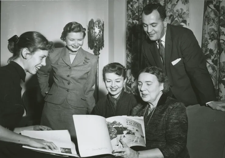 Dr. Pauline Beery Mack seated with a group of people, reading Teen-age Food Patterns.