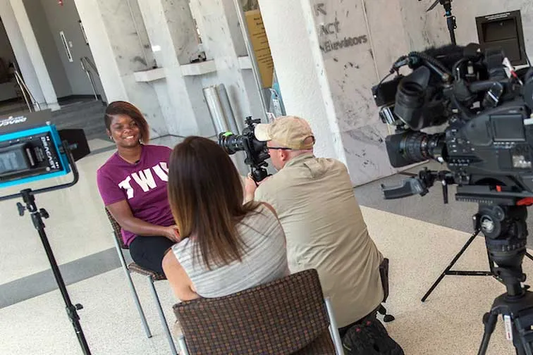A student wearing a TWU t-shirt sits in front of a camera during an interview.