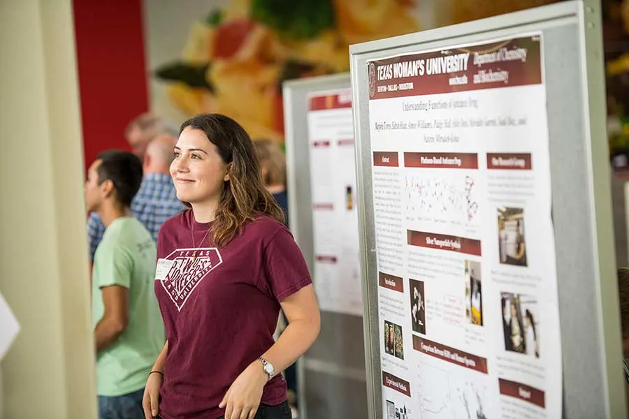 A TWU student stands in front of her research poster at an event.