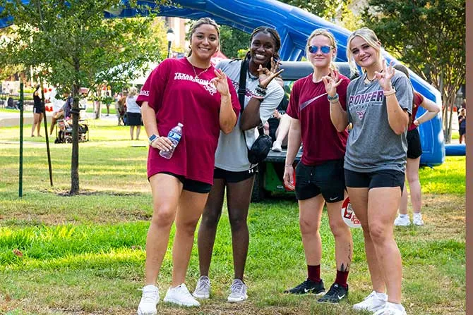 A group of four TWU students at an event and holding up the TWU hand sign to the camera.