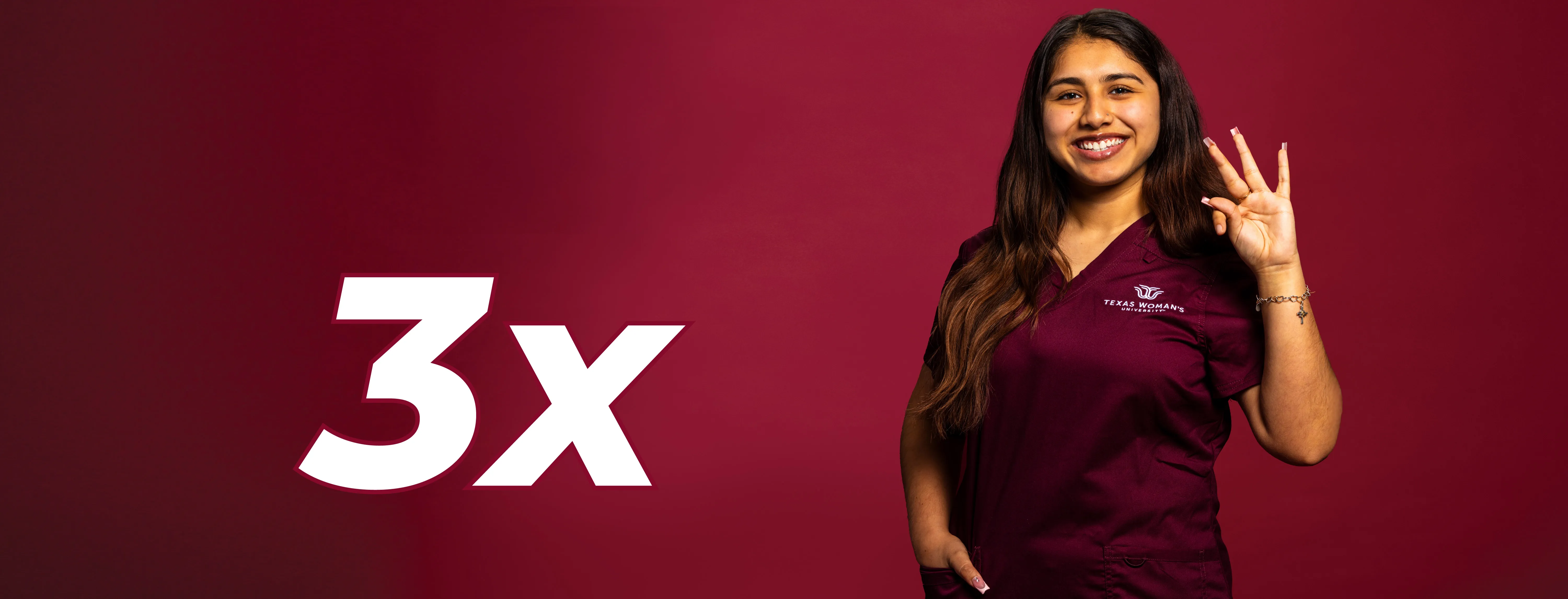 A TWU student in maroon scrubs holding up the TWU hand sign with 