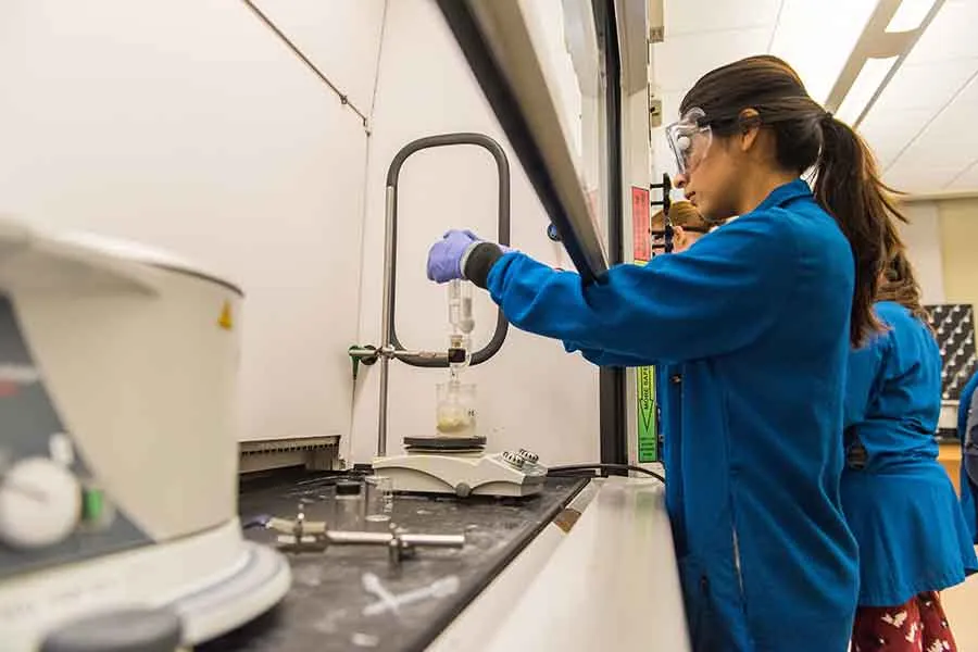 A young woman in safety gear working in a chemistry lab.