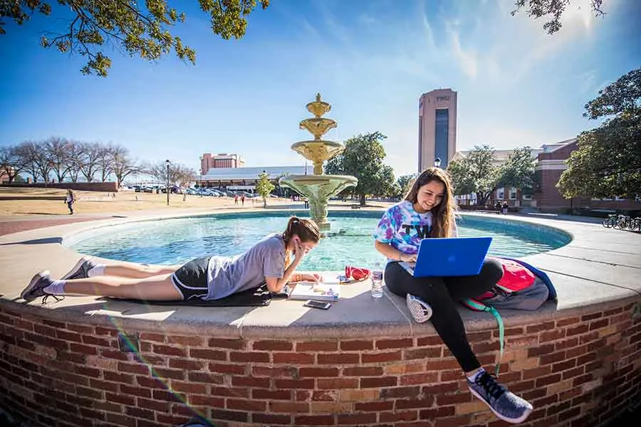 Two TWU students study on the Denton campus fountain.