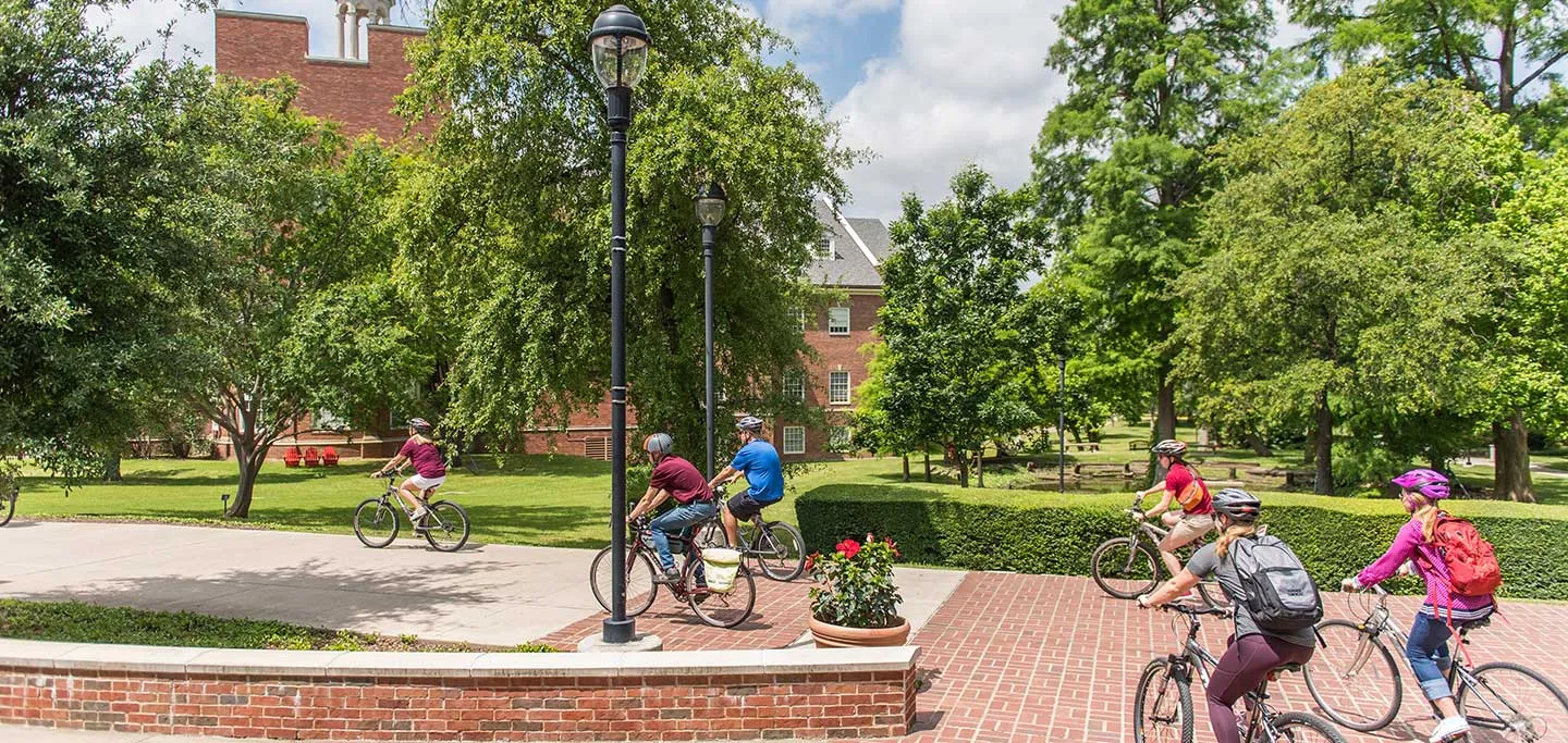 A view of TWU's Denton campus on a sunny day with a string of bikers using a bike path.
