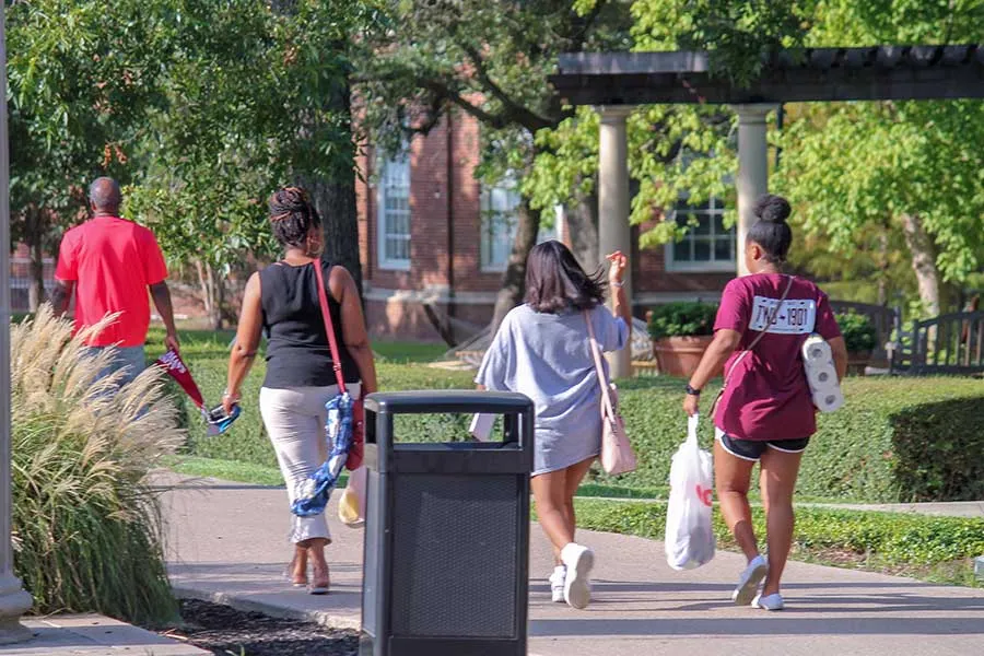 Students and family walk away from camera while carrying room supplies on move-in day 2019.
