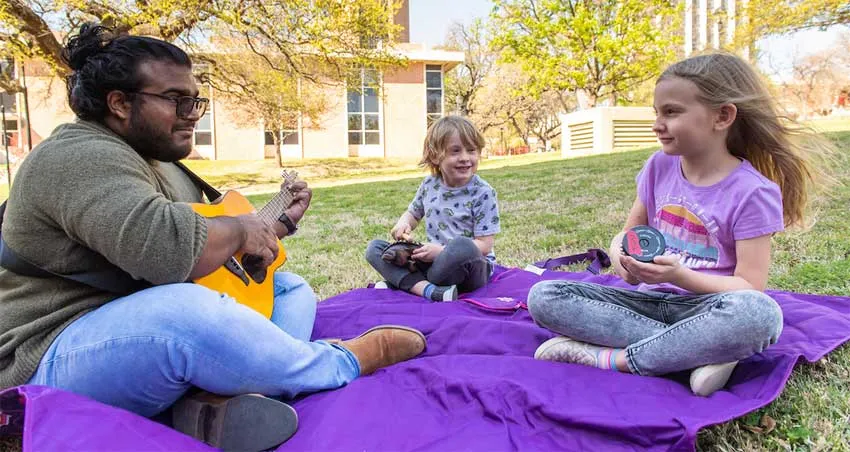 TWU Music Therapy student Abel Abraham works with children outside of Margo Jones Performance Hall.  