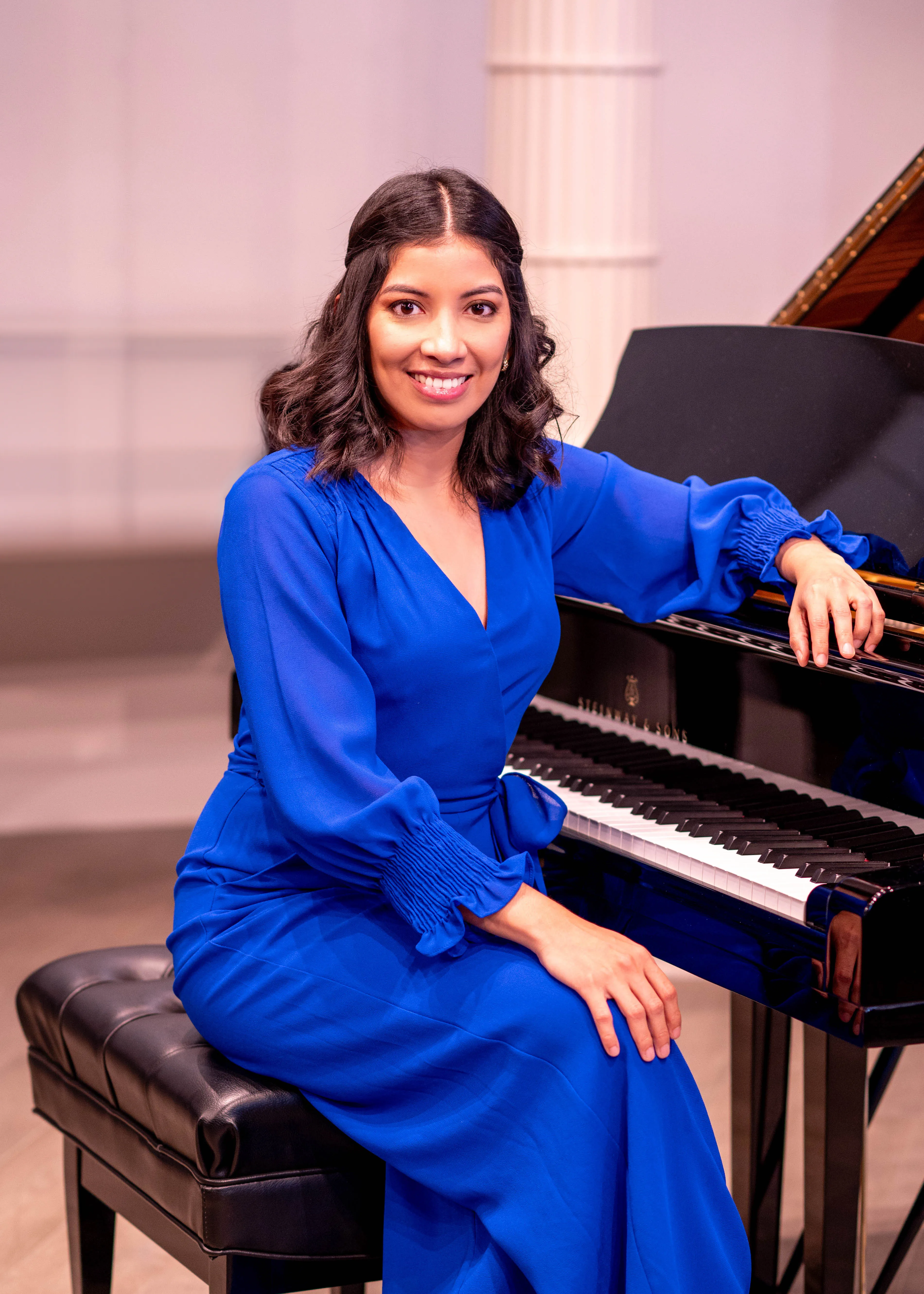 Fanarelia in a blue dress sitting at a grand piano