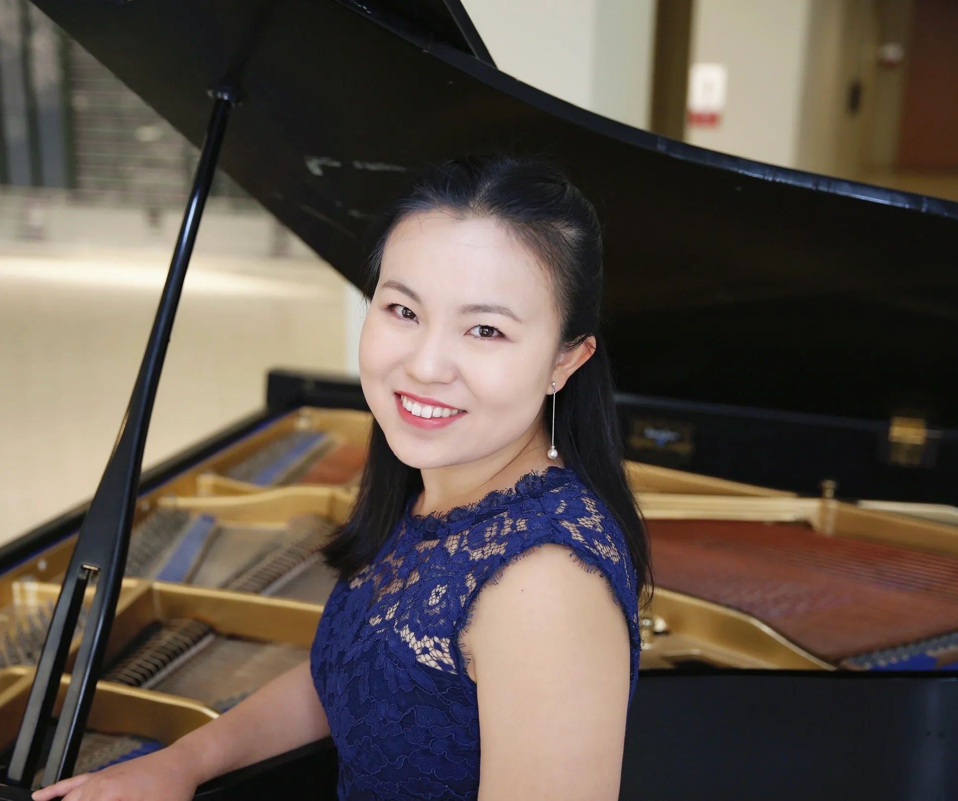 Hongling Liang stands in front of a piano wearing a navy blue dress