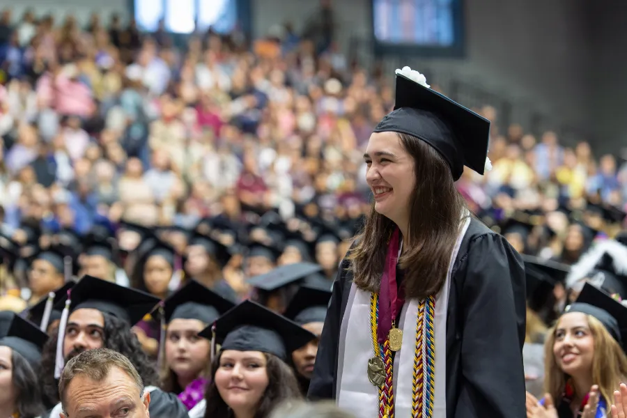 A graduate standing at commencement wearing a cap and gown