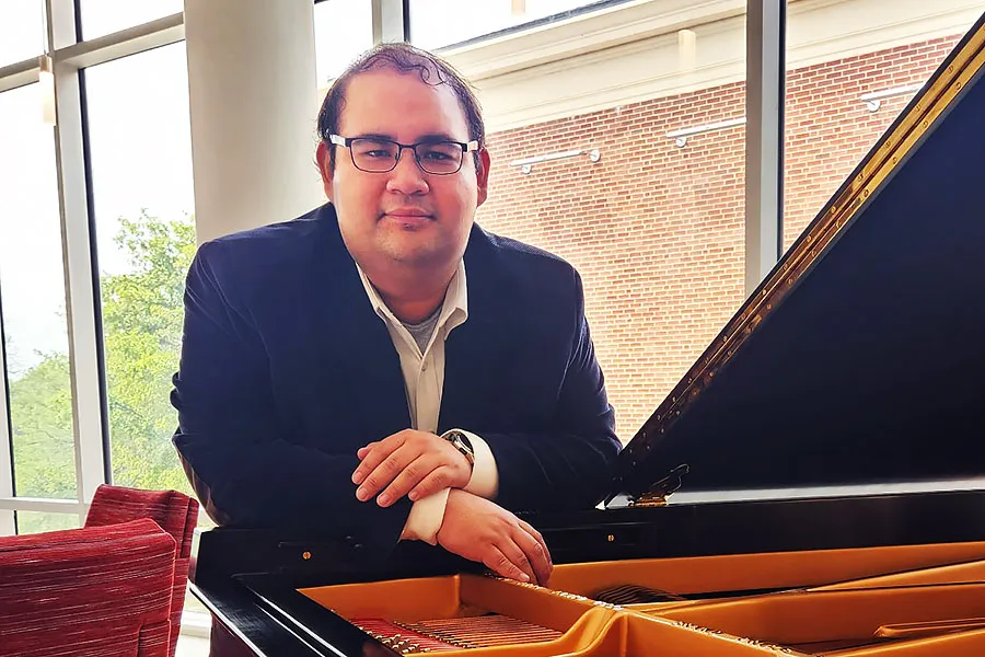 Alexis Martinez leans against a grand piano