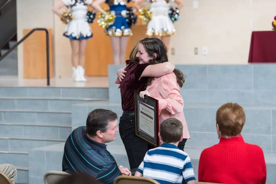 Caroline Deitch hugs her high school teacher in her high school auditorium.