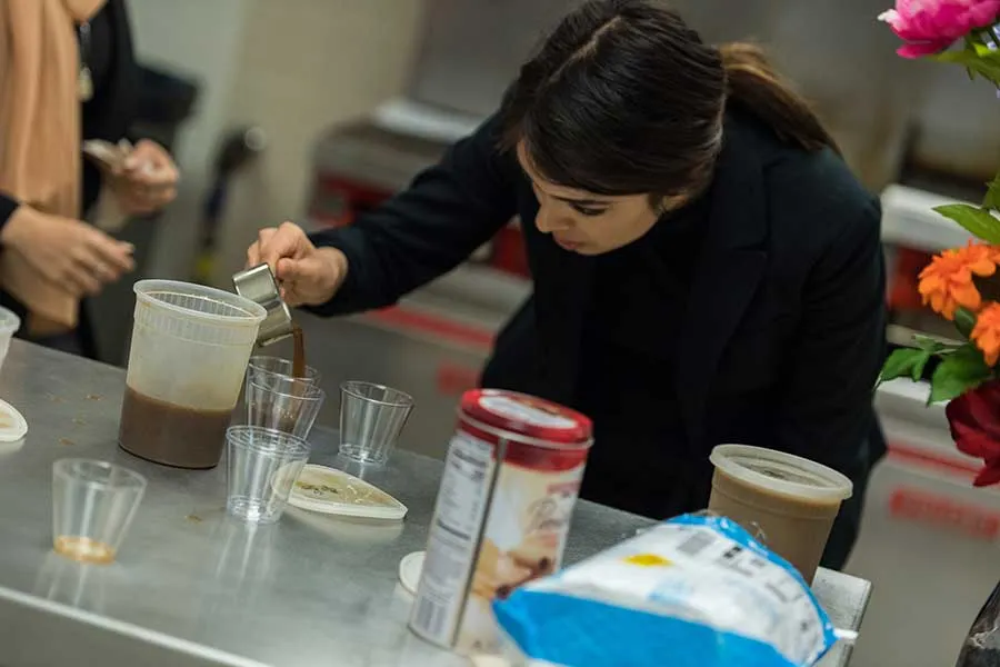 Shiraz Soltani plates her teams protein coffee product in an industrial kitchen setting.