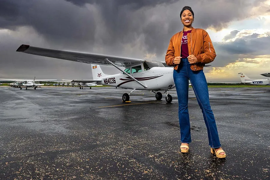 A ɫƵ aviation student stands in front of a plane on a tarmac