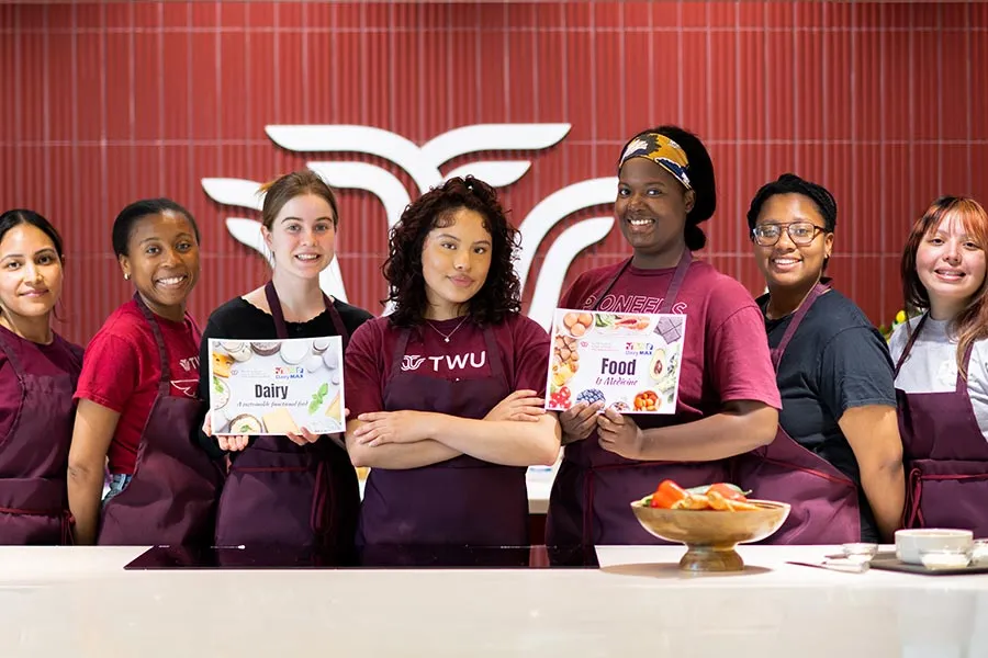 seven students in maroon aprons stand behind a counter in the Wellness Kitchen