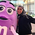 a TWU alum stands next to a person in a purple M&M costume