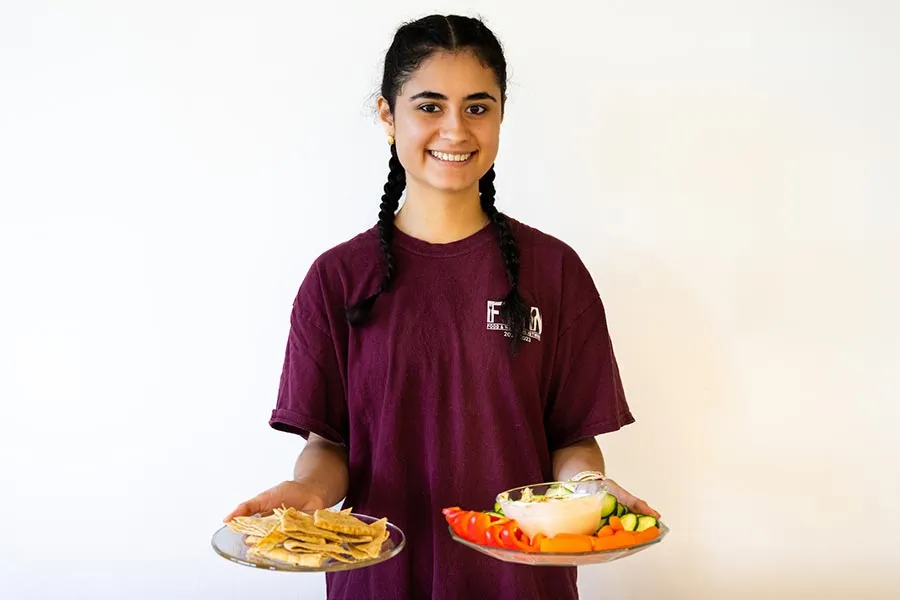 ̽¥ student Mariana Salazar holds two plates with food in front of a white backdrop