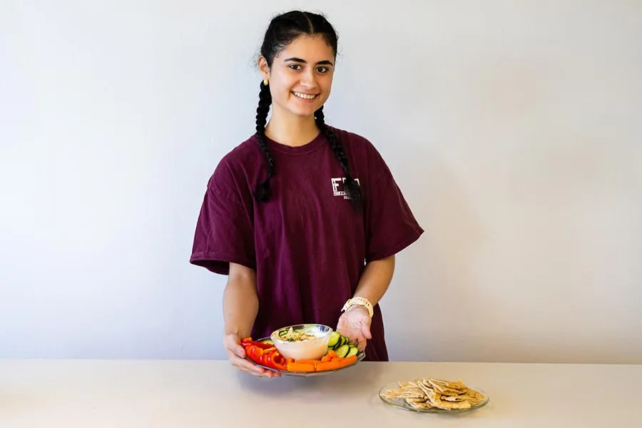 TWU dietetics student Mariana Salazar holds a plate of food in front of a white background
