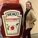 Rachel Russell smiling and posing next to a giant Heinz ketchup bottle.