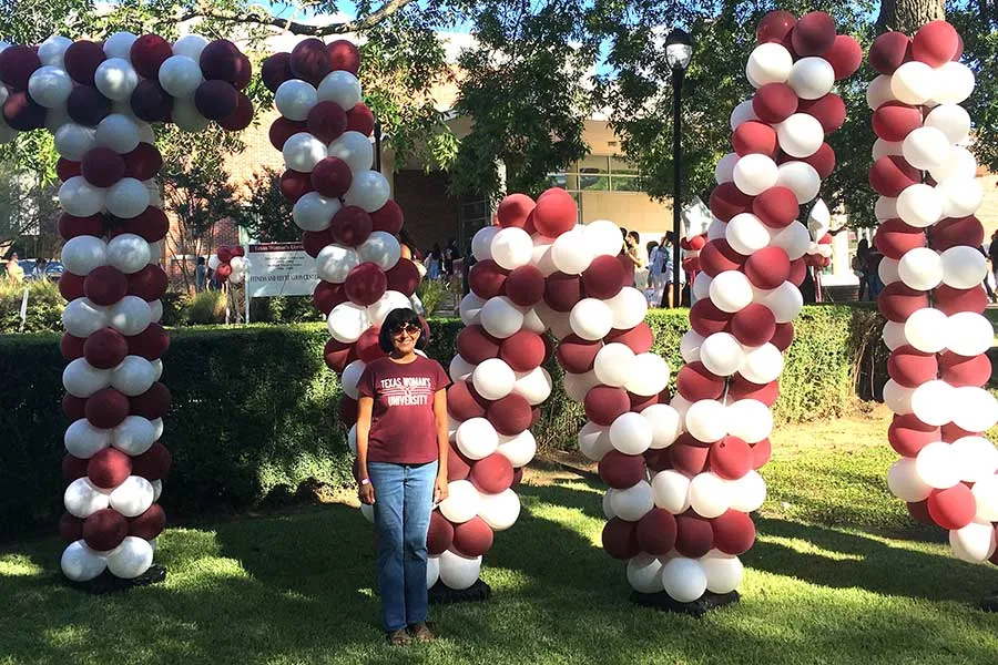 student stands in front of TWU sign made up of maroon and white balloons 