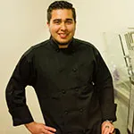 Walter Rivas in a chef uniform and posing in a kitchen setting.