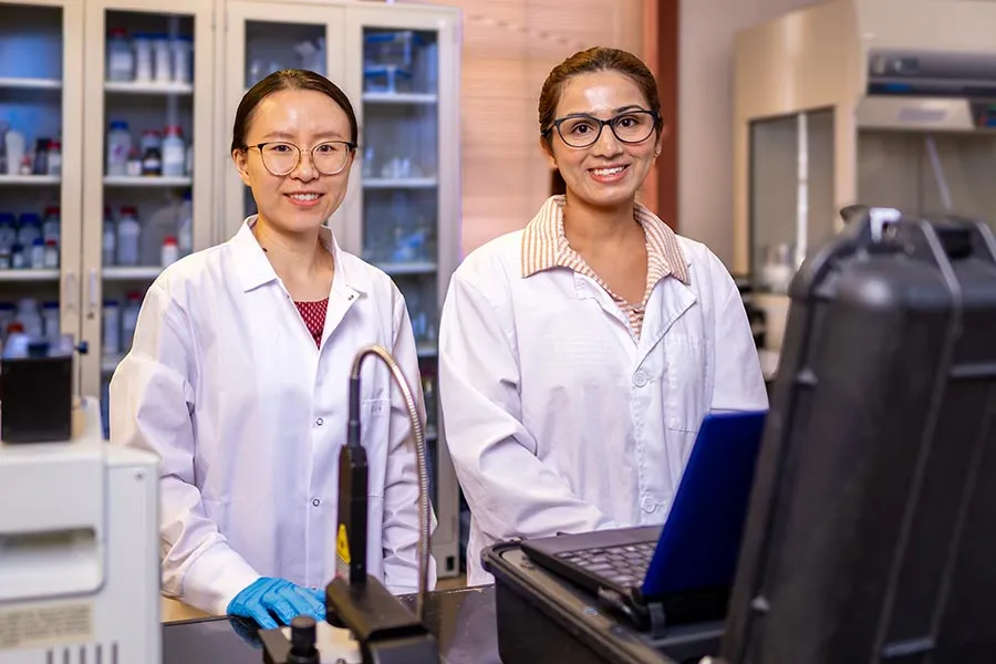 Dr. Wang stands next to PhD student in lab with white lab coats