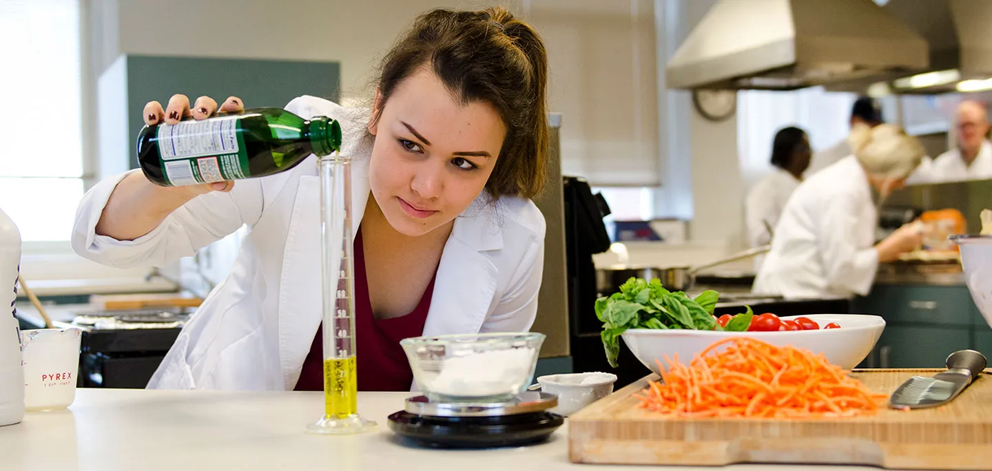 A culinology student measures olive oil into a narrow beaker