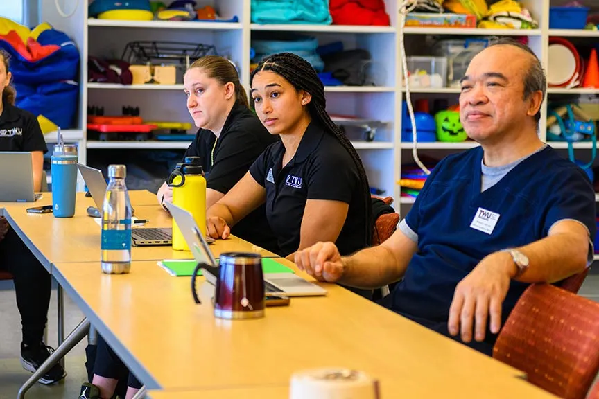 a faculty member sits at a table with four students sitting around the table
