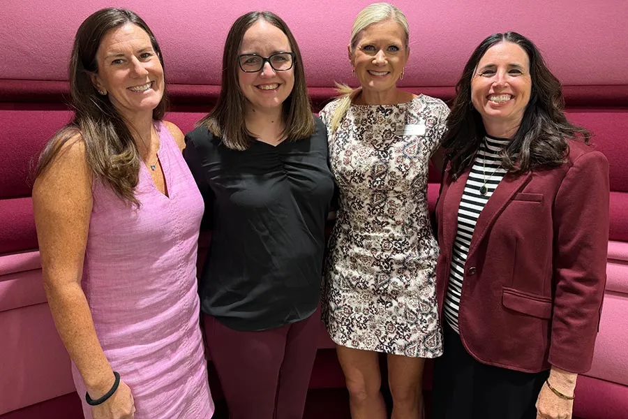 four TWU faculty members stand together in front of a pink an maroon background