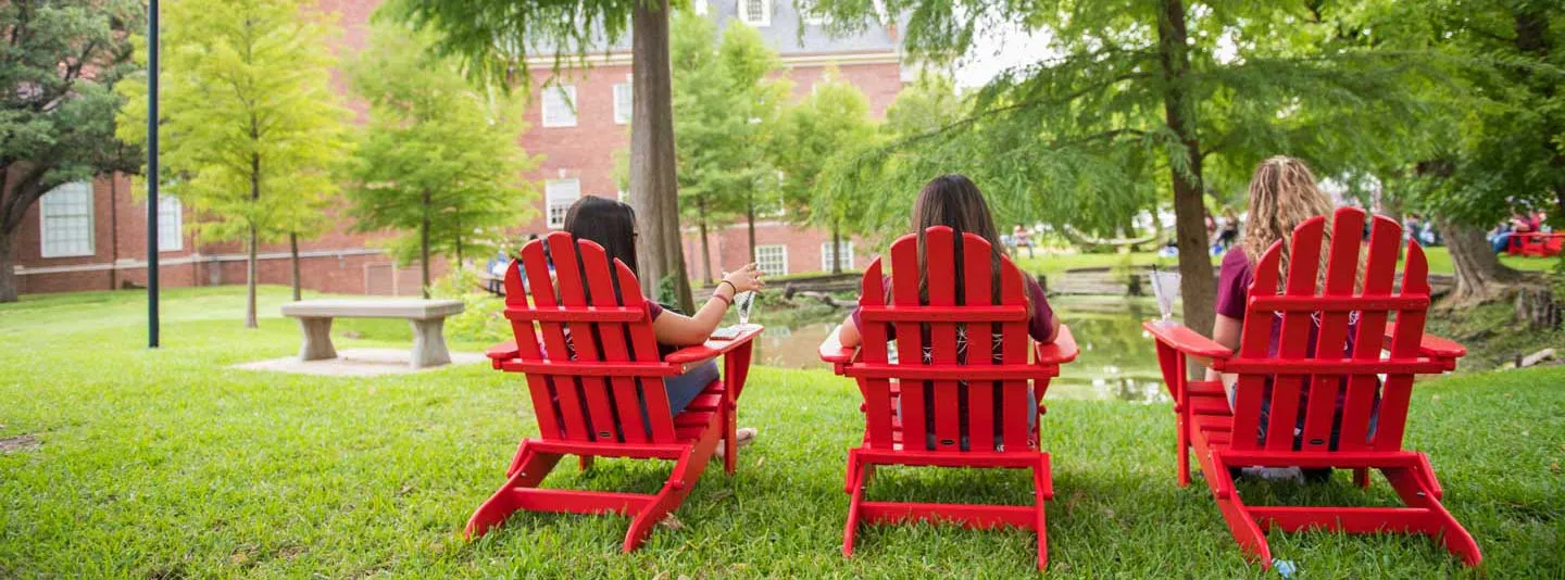 Three students sit in lounge chairs outdoors on TWU's Denton campus
