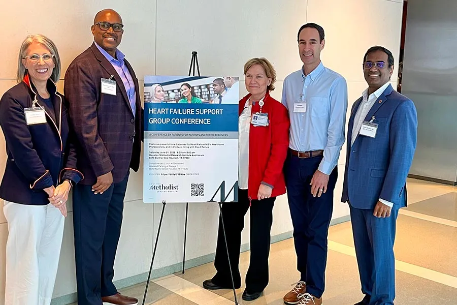 five people in professional attire stand next to a poster promoting a heart failure support group conference